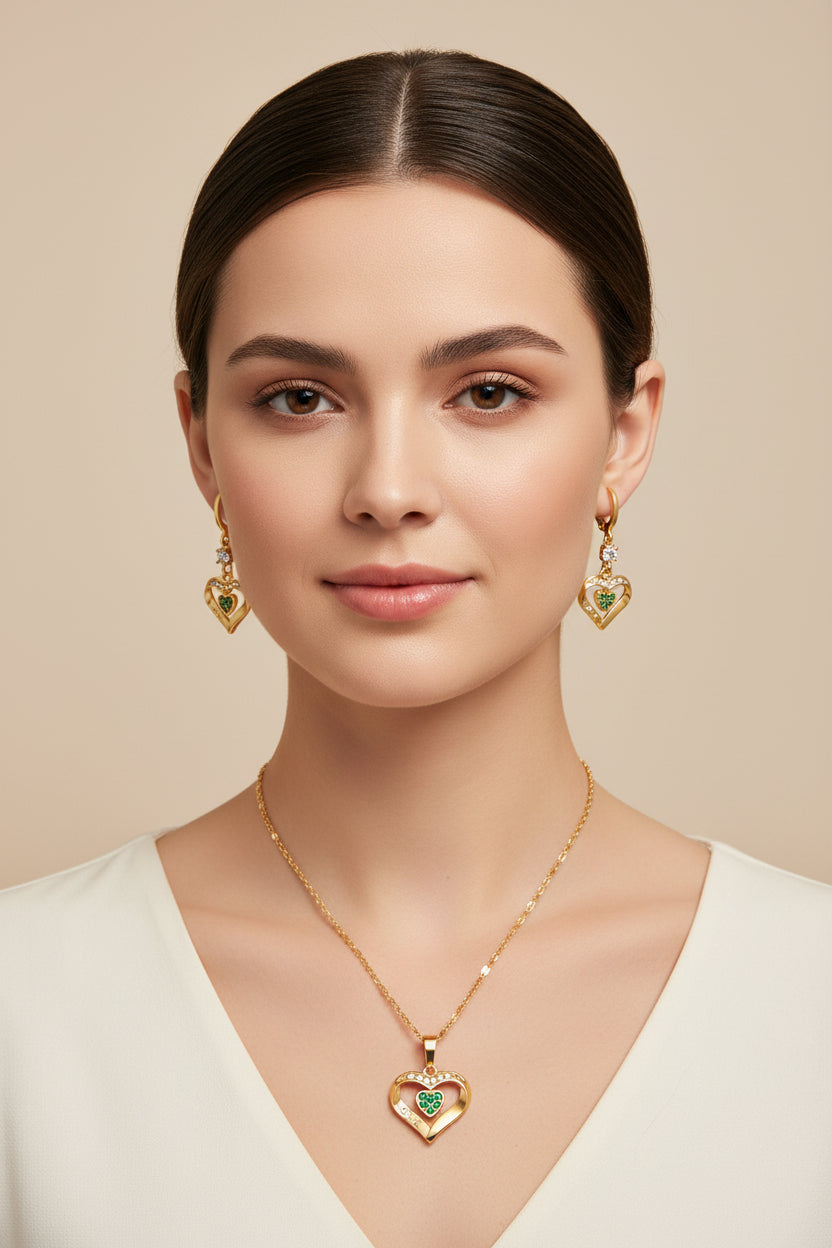 Gold heart-shaped jewelry set with green stones and 'LOVE' engraving on a white background.