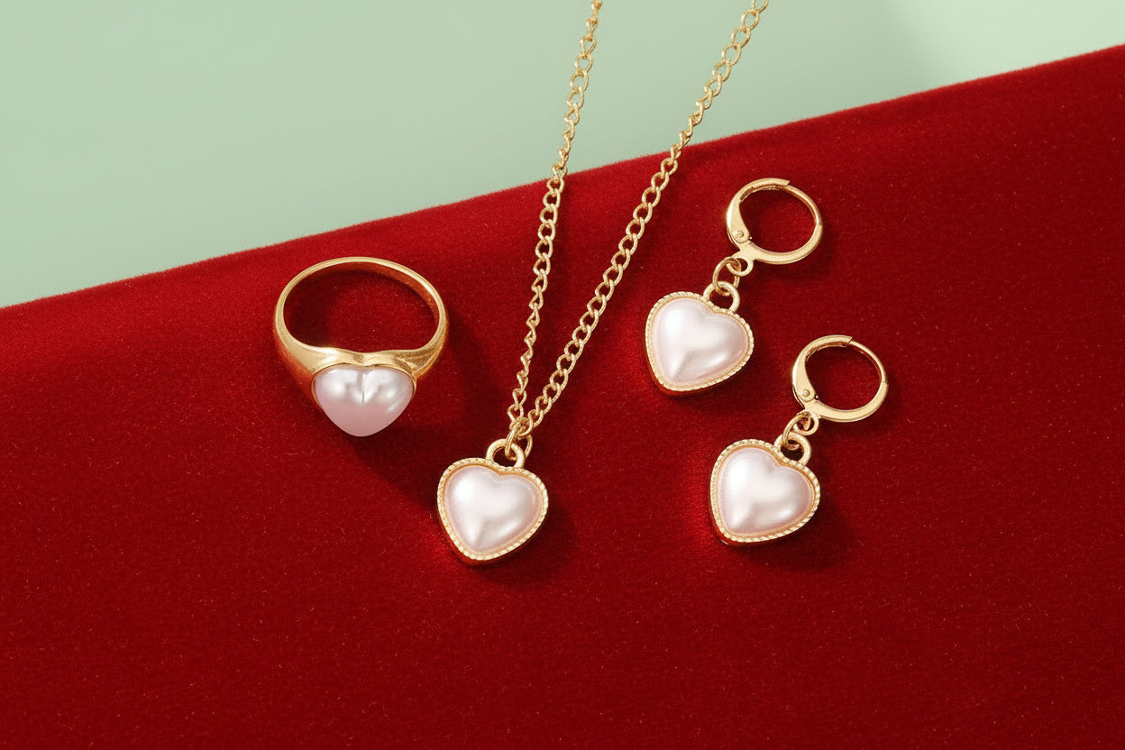 Gold jewelry set with heart-shaped pearl charms on a black surface.