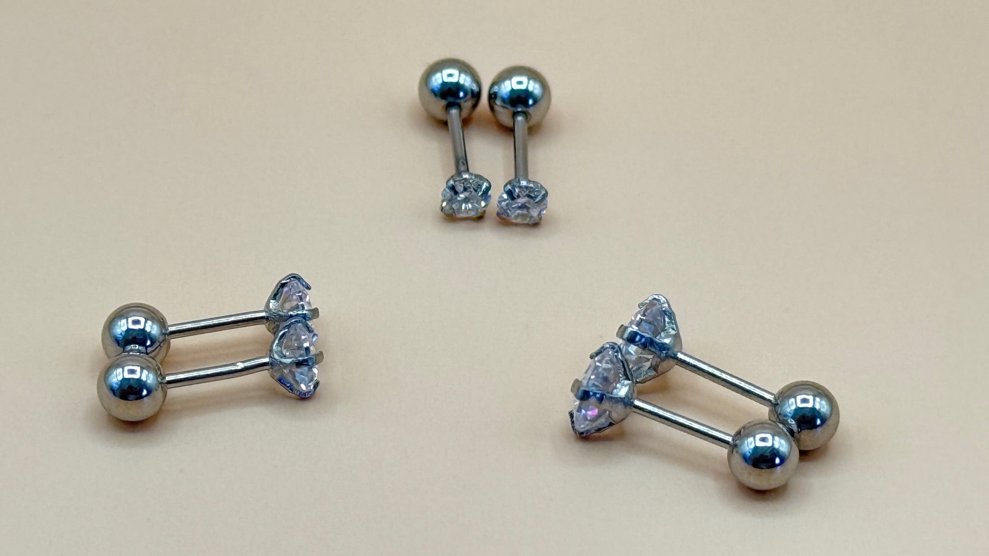 Pair of silver belly button rings with clear gemstones on a beige background