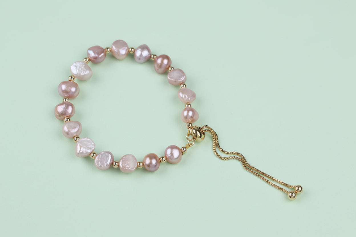 Pearl bracelet with gold chain on a light pink background