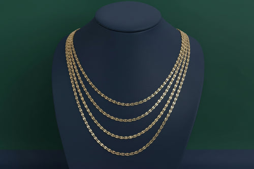 Gold chain necklace on a black mannequin bust against a plain background