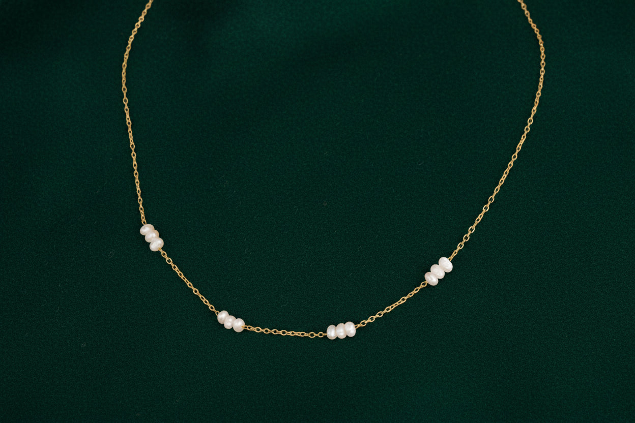 Gold necklace with pearls worn by a person, close-up on neck and shoulder.
