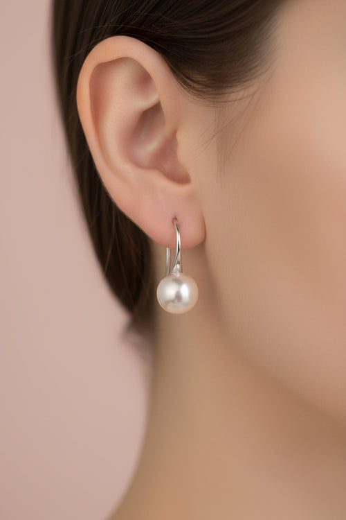 Pearl earrings on a dark surface with a blurred gold object in the background