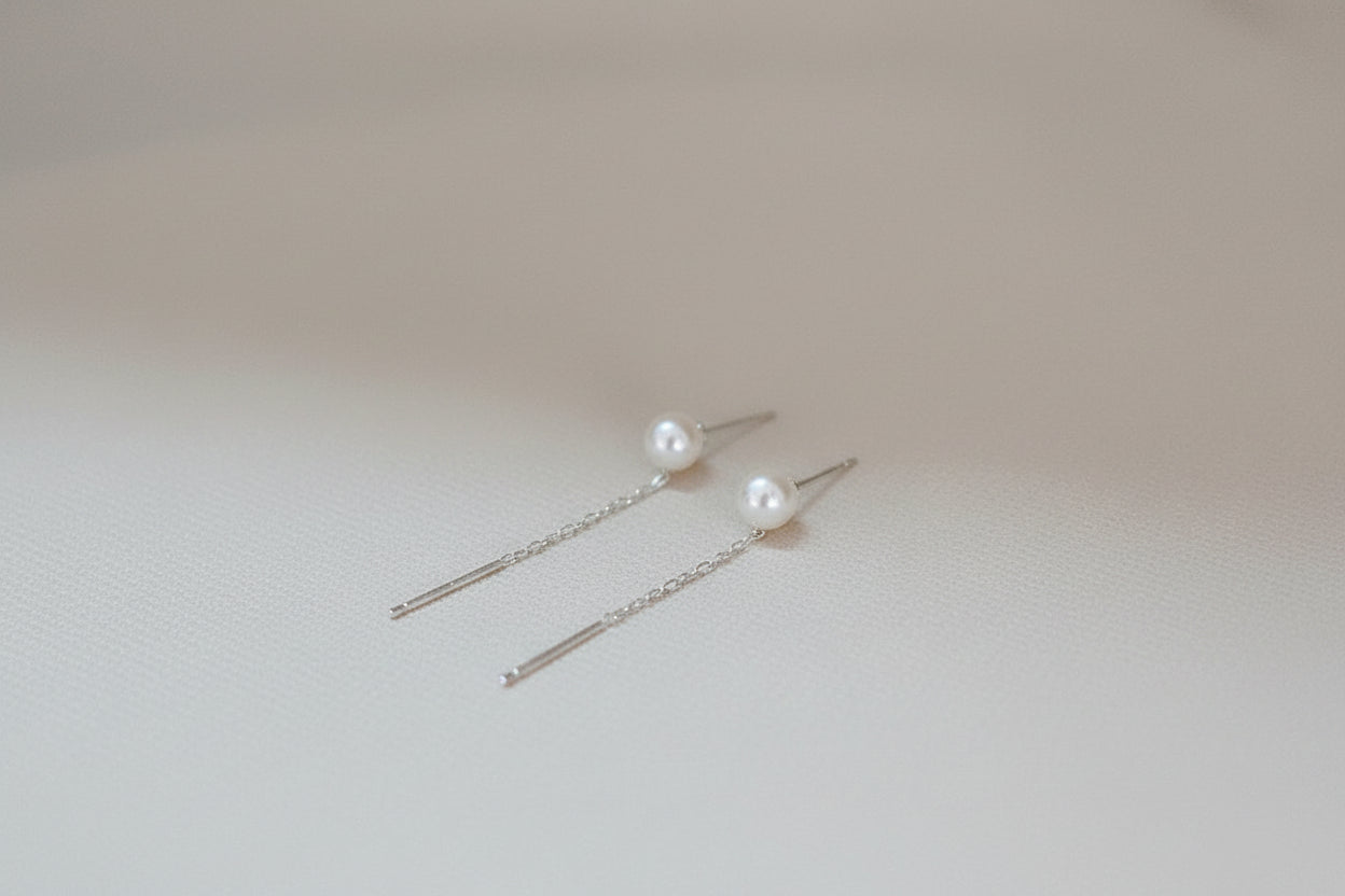 Pearl earrings held between fingers on a plain background