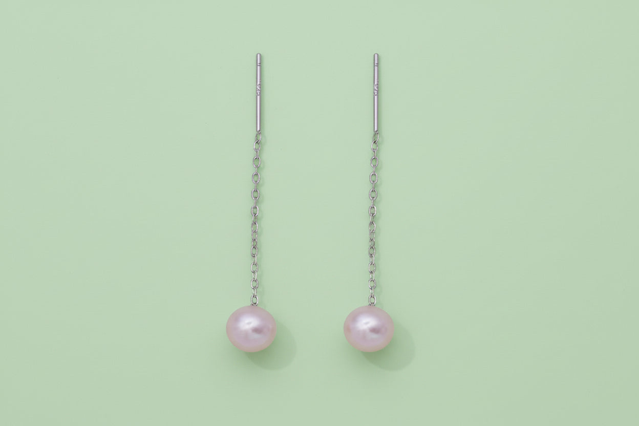 Pair of pearl drop earrings on thin silver chains against a white background